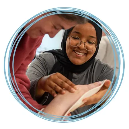 An O T student smiles as she practices placing a malleable splint on another student